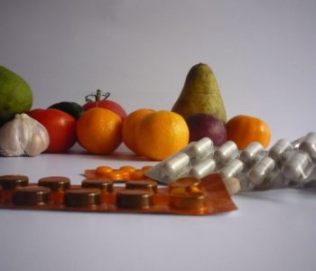 Vitamine Tabletten im Vordergrund und Obst, Apfel, Birne, Orange, Tomate, Knoblauch im Hintergrund